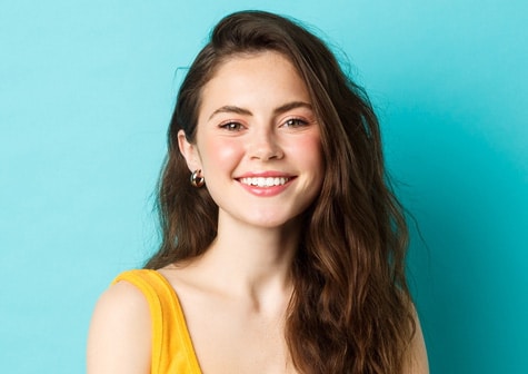 Smiling woman in a yellow shirt against a turquoise background.